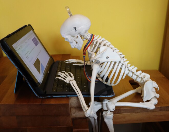 Model skeleton hunched up over its laptop