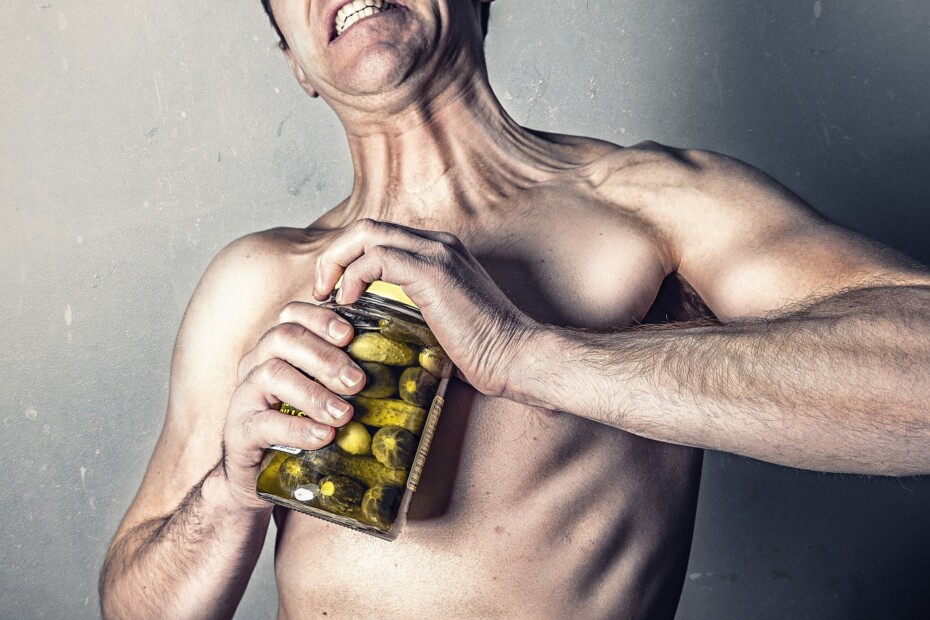 Photo of man trying to open a jar of pickles and looking like it's really hard work
